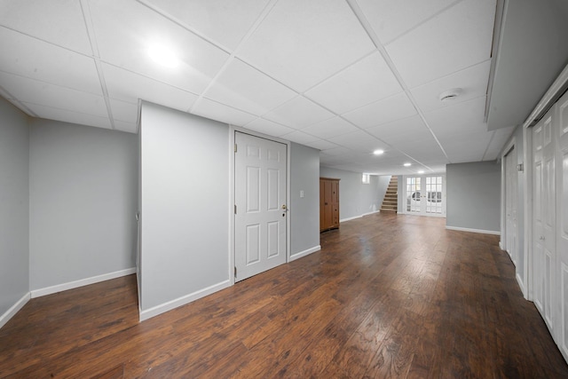 finished below grade area with stairway, baseboards, dark wood-style floors, and a paneled ceiling