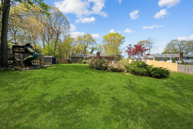 view of yard with fence, an outdoor structure, a playground, and a shed