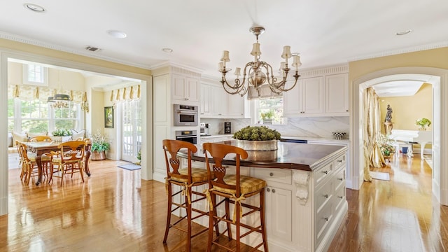 kitchen featuring visible vents, light wood-style floors, backsplash, an inviting chandelier, and crown molding