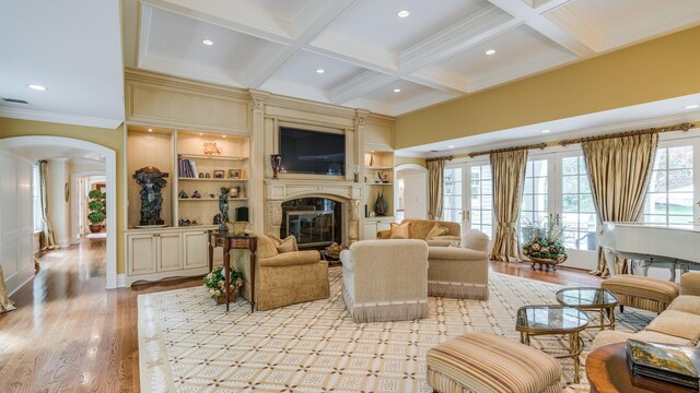 living area with arched walkways, coffered ceiling, a fireplace, light wood-type flooring, and beam ceiling