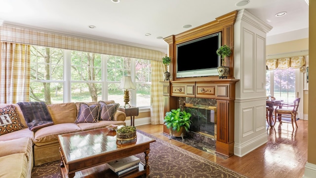 living room featuring light wood finished floors, recessed lighting, a premium fireplace, ornamental molding, and baseboards