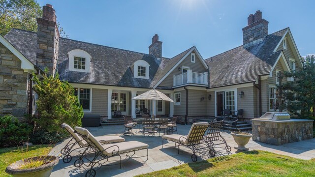 back of house with entry steps, a balcony, a chimney, exterior kitchen, and a patio area