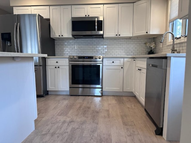 kitchen with stainless steel appliances, light countertops, light wood-style floors, white cabinetry, and tasteful backsplash