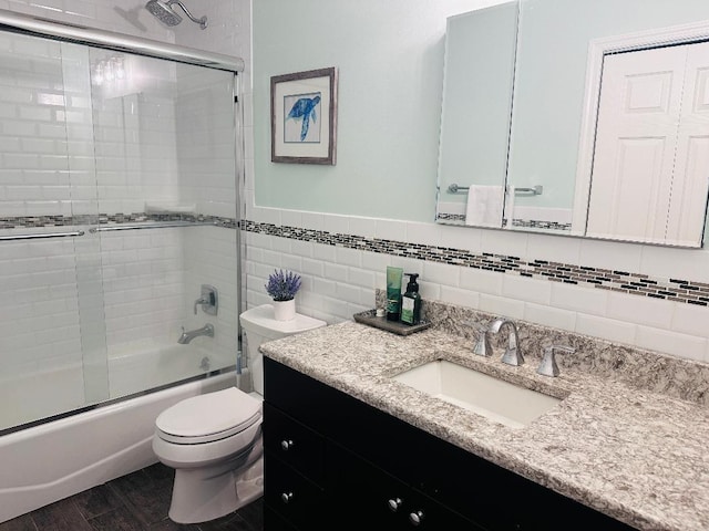 bathroom featuring toilet, wood finished floors, combined bath / shower with glass door, tile walls, and vanity