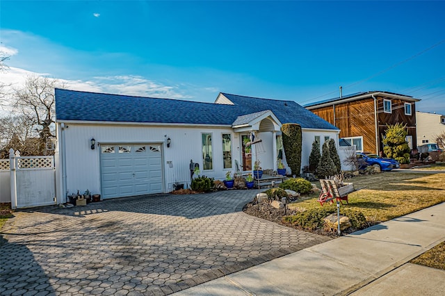 ranch-style home featuring a garage, a shingled roof, fence, and decorative driveway