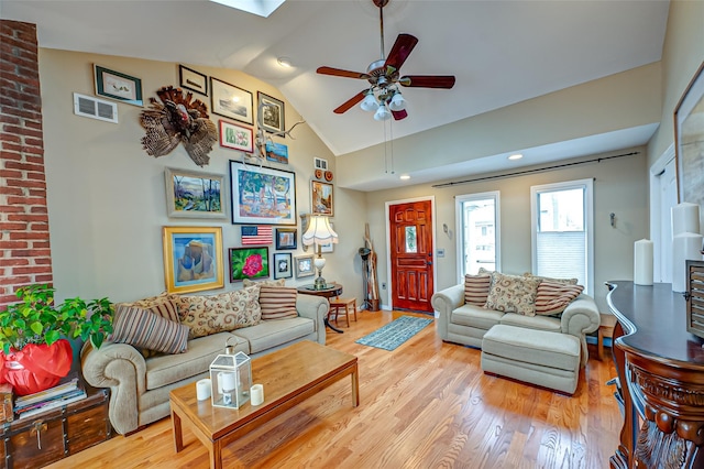 living area with lofted ceiling with skylight, light wood-style flooring, visible vents, and a ceiling fan