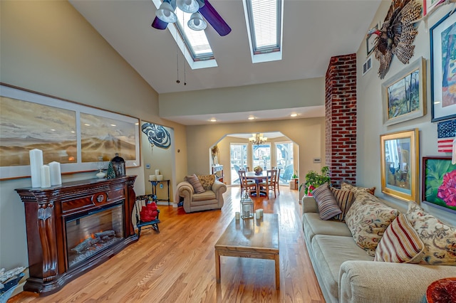 living room with arched walkways, high vaulted ceiling, wood finished floors, visible vents, and a glass covered fireplace