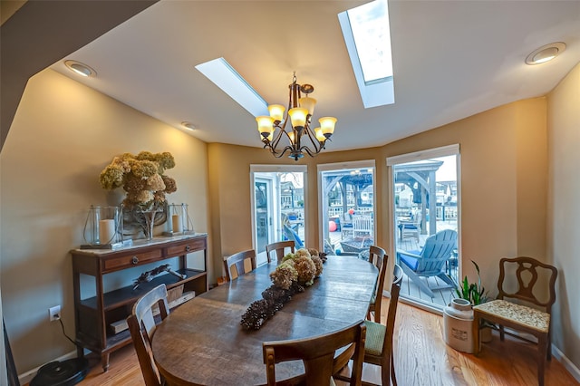 dining area with a skylight, light wood finished floors, and a notable chandelier