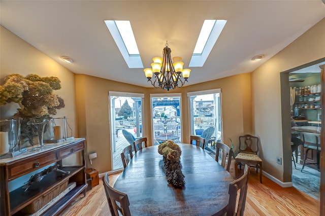 dining room with lofted ceiling with skylight, light wood-type flooring, a chandelier, and baseboards