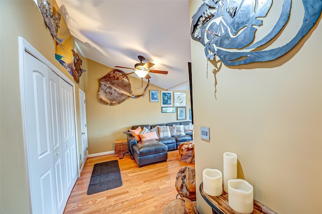 living area with light wood-type flooring, ceiling fan, baseboards, and vaulted ceiling