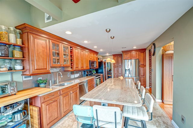 kitchen with light stone counters, stainless steel appliances, a sink, visible vents, and brown cabinets