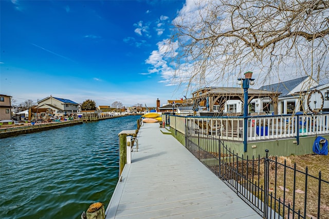 view of dock featuring a water view, a residential view, and fence