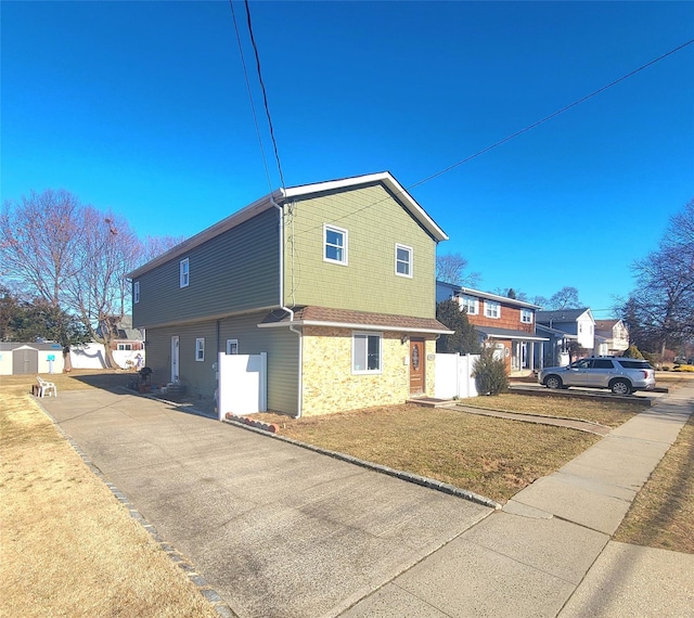 view of property exterior with stone siding, fence, aphalt driveway, and a yard