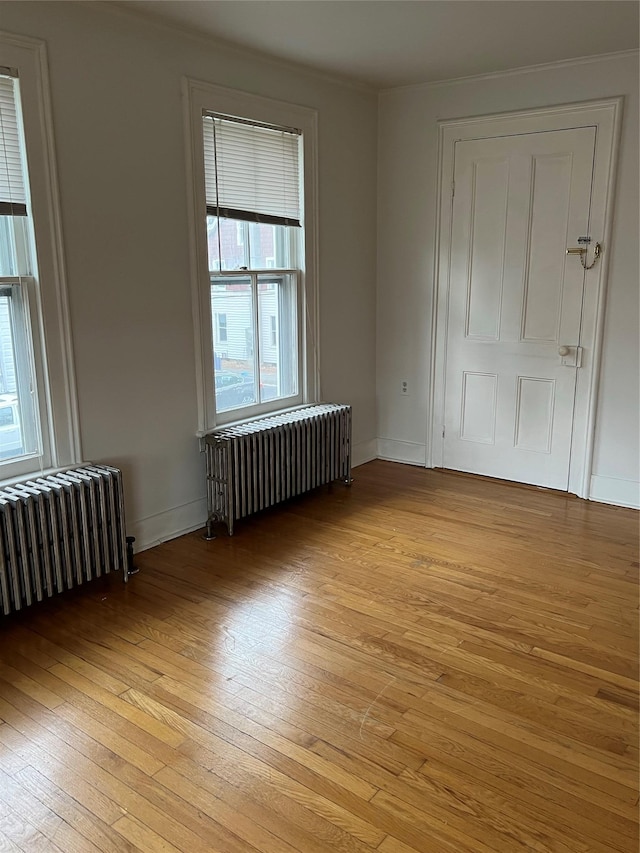 empty room featuring radiator, light wood-style flooring, and baseboards