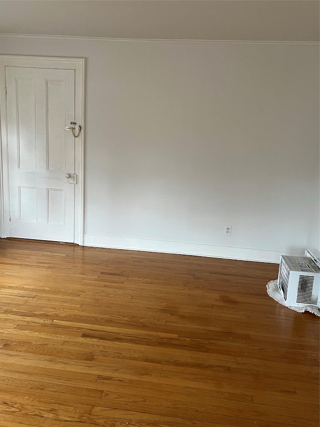 unfurnished room featuring a wall unit AC, crown molding, baseboards, and wood finished floors