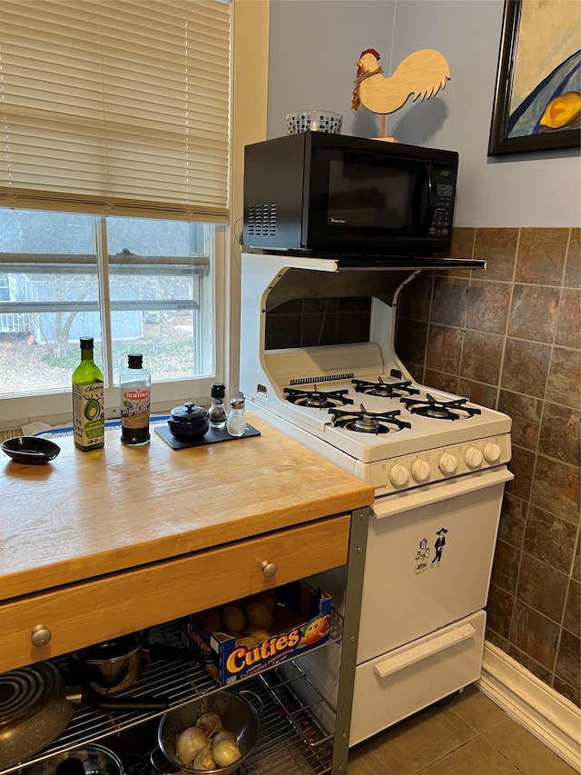 kitchen with black microwave, light countertops, tile walls, and white gas stove