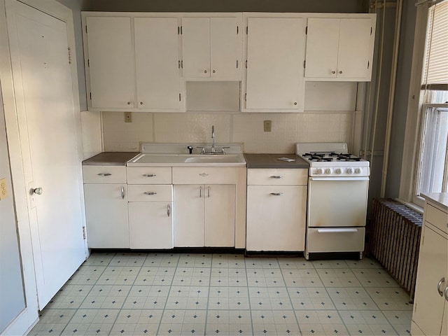 kitchen with light floors, tasteful backsplash, white cabinetry, a sink, and white range with gas stovetop