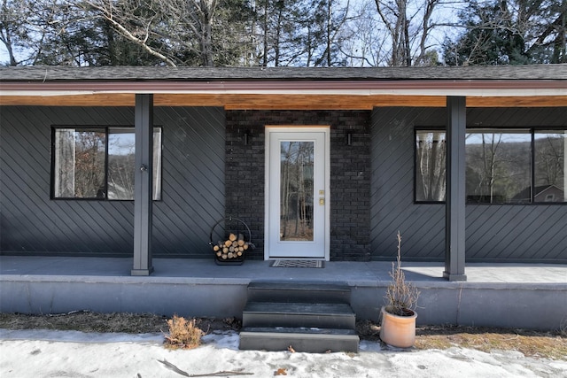 entrance to property featuring covered porch and roof with shingles