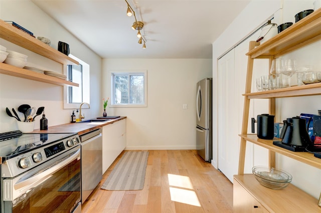 kitchen with light wood-type flooring, open shelves, a sink, stainless steel appliances, and baseboards