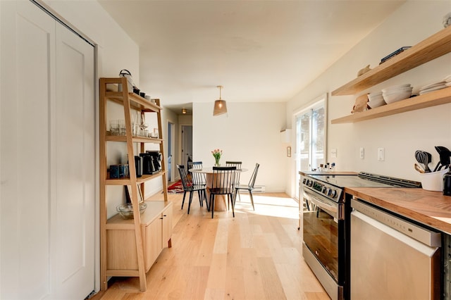 kitchen featuring light wood-type flooring, butcher block countertops, open shelves, decorative light fixtures, and appliances with stainless steel finishes