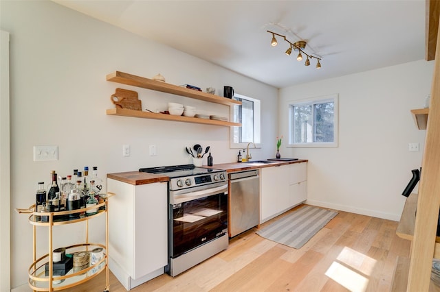 kitchen with light wood finished floors, butcher block counters, appliances with stainless steel finishes, white cabinetry, and a sink