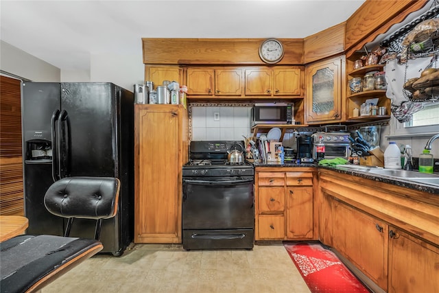 kitchen featuring dark countertops, black appliances, brown cabinetry, and a sink