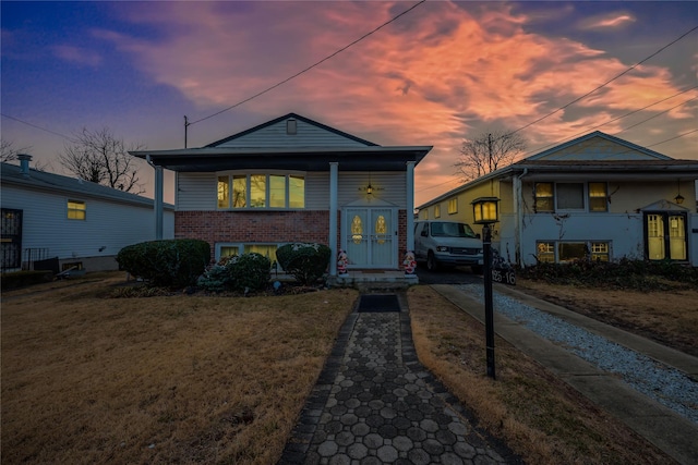 view of front of property with a yard, driveway, brick siding, and french doors