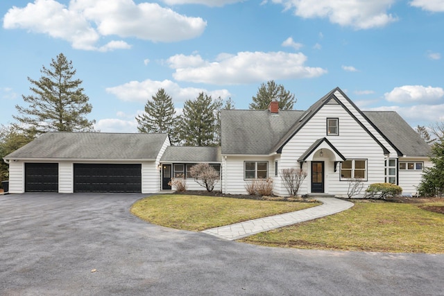 view of front of property featuring aphalt driveway, a garage, roof with shingles, a front lawn, and a chimney