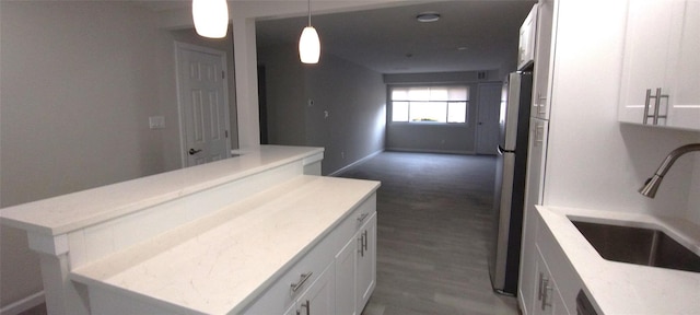 kitchen with freestanding refrigerator, white cabinets, a sink, and a center island