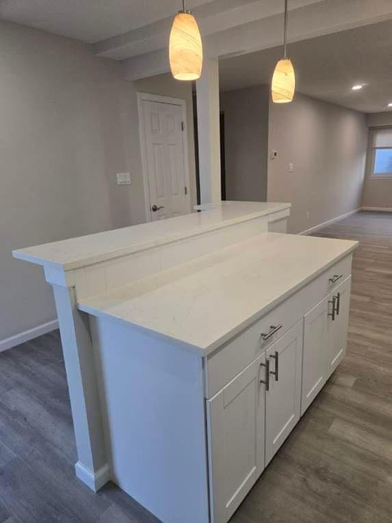 kitchen with a center island, decorative light fixtures, white cabinets, wood finished floors, and baseboards