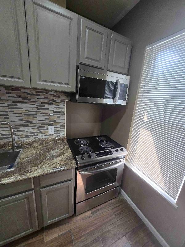 kitchen with baseboards, decorative backsplash, appliances with stainless steel finishes, wood finished floors, and a sink