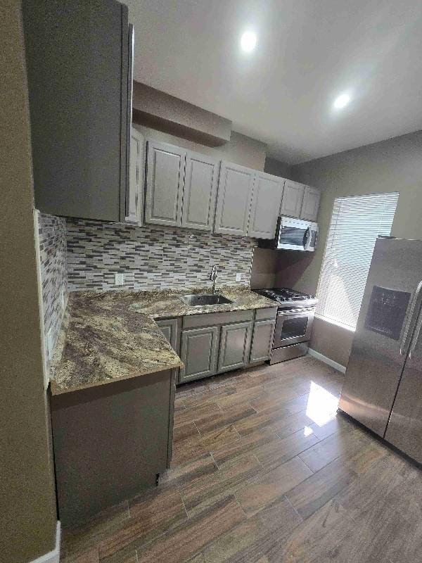 kitchen with backsplash, gray cabinets, dark wood-style floors, stainless steel appliances, and a sink