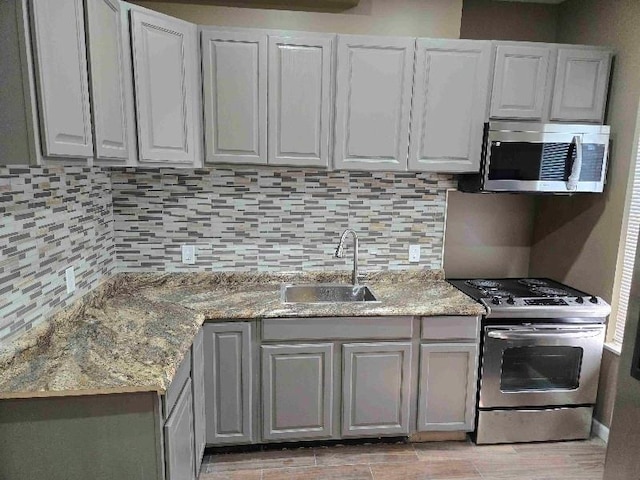 kitchen with backsplash, appliances with stainless steel finishes, light stone countertops, and a sink