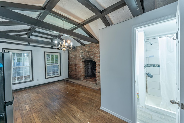 unfurnished living room with lofted ceiling with beams, hardwood / wood-style floors, an inviting chandelier, a brick fireplace, and baseboards