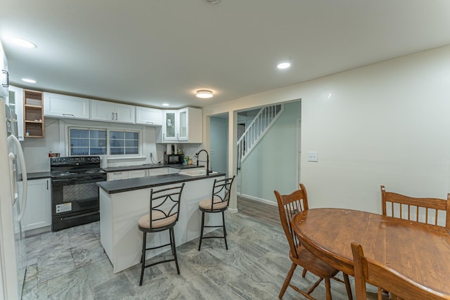 kitchen with dark countertops, white cabinetry, a sink, black appliances, and a kitchen bar