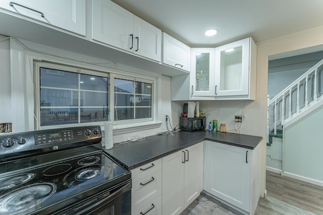 kitchen featuring black range with electric cooktop, dark countertops, white cabinetry, and glass insert cabinets