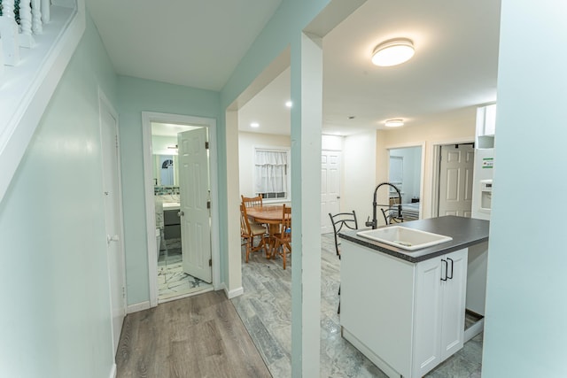 interior space featuring a sink, baseboards, white cabinets, light wood finished floors, and dark countertops