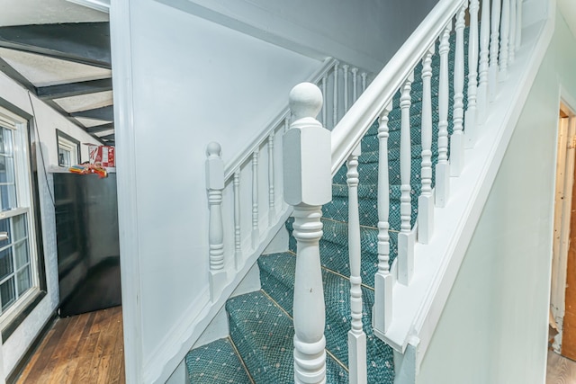 staircase with beamed ceiling and wood finished floors