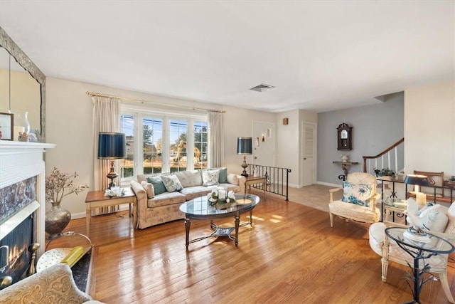 living area featuring light wood-style flooring, a fireplace, visible vents, baseboards, and stairway