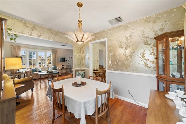 dining room with wood finished floors, visible vents, baseboards, and wallpapered walls