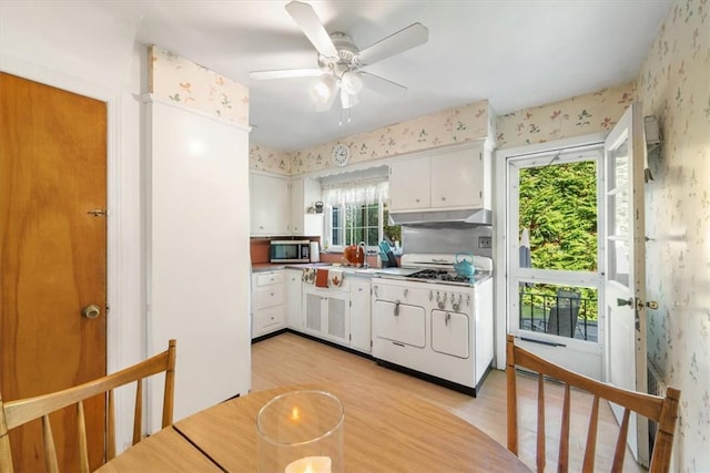 kitchen with white gas stove, stainless steel microwave, wallpapered walls, and under cabinet range hood