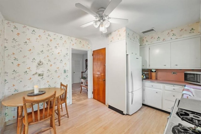 kitchen with wallpapered walls, light wood finished floors, visible vents, stainless steel microwave, and white cabinetry