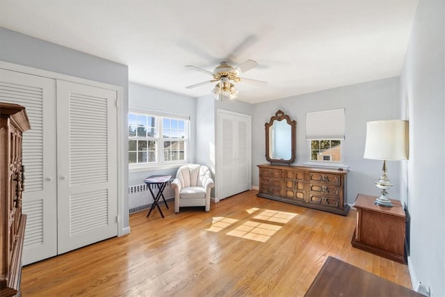 bedroom featuring radiator, ceiling fan, two closets, and wood finished floors