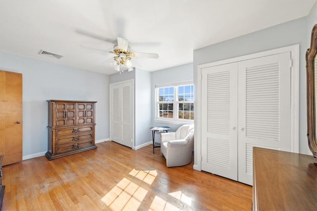 bedroom featuring light wood finished floors, baseboards, visible vents, a ceiling fan, and two closets