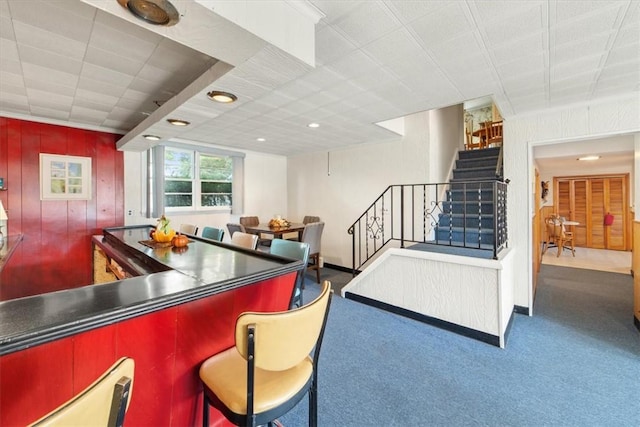 bar featuring carpet, wooden walls, a bar, and stairs