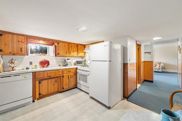 kitchen with a wainscoted wall, white appliances, wood walls, light countertops, and brown cabinets