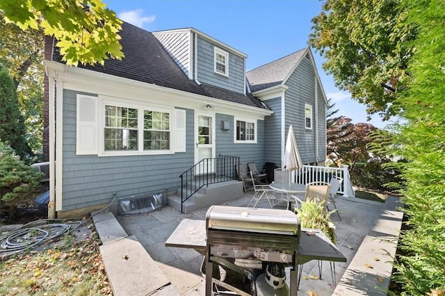 back of property with a shingled roof and a patio area