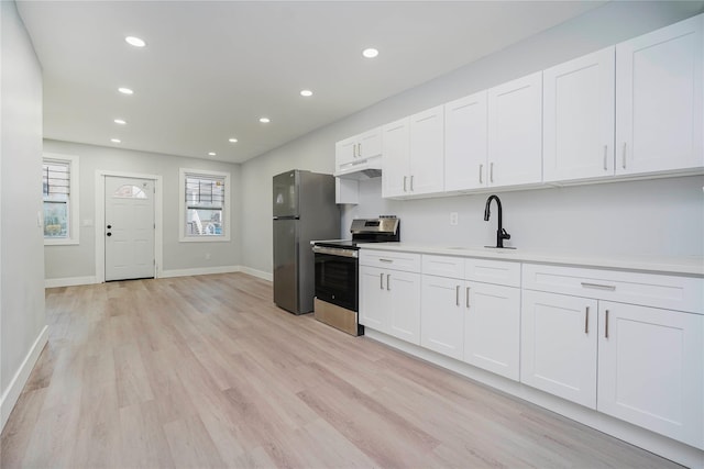 kitchen featuring light wood-style flooring, a sink, stainless steel appliances, white cabinets, and under cabinet range hood