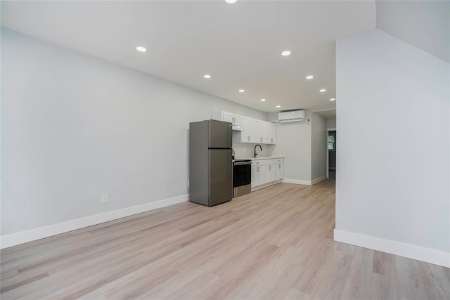 kitchen featuring baseboards, stainless steel appliances, an AC wall unit, light countertops, and white cabinetry