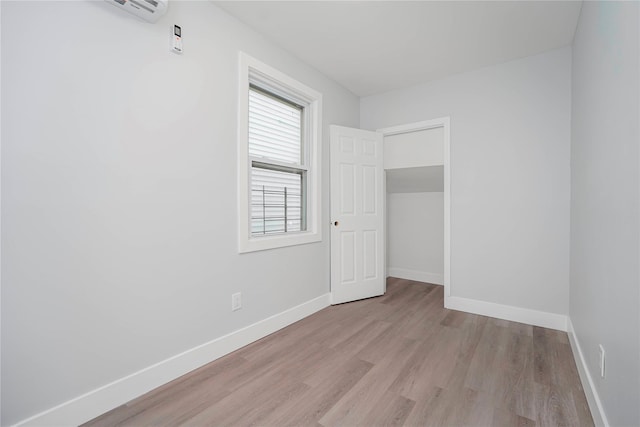 empty room featuring a wall unit AC, baseboards, and wood finished floors